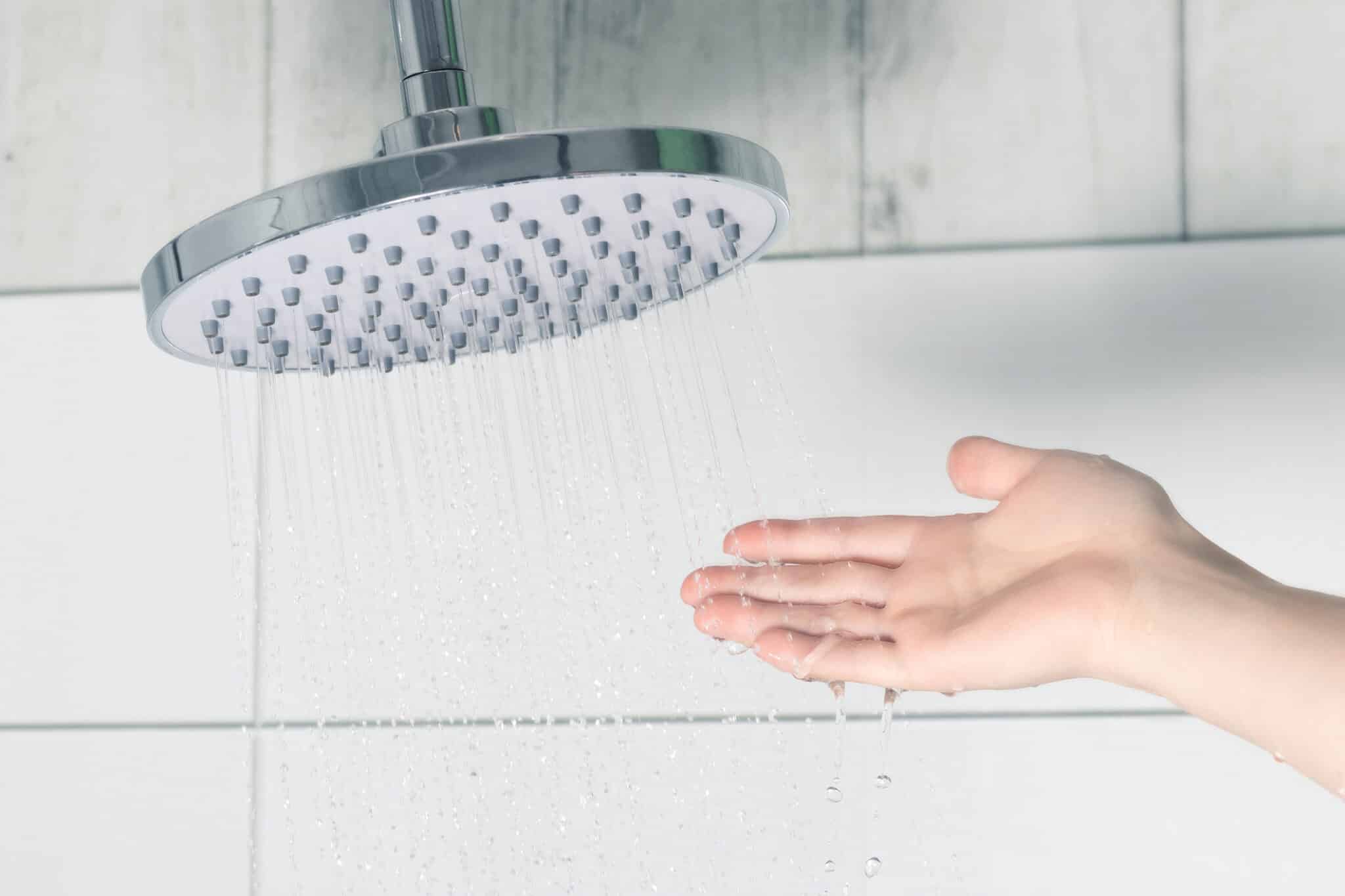Female hand touching water pouring from a rain shower head, checking water temperature, Optimal Shower Pressure.